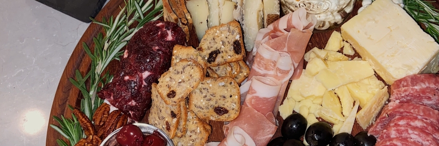 A round platter of cold cut meats, cheeses, produce, mixed nuts, olives and popcorn bordered with rosemary.
